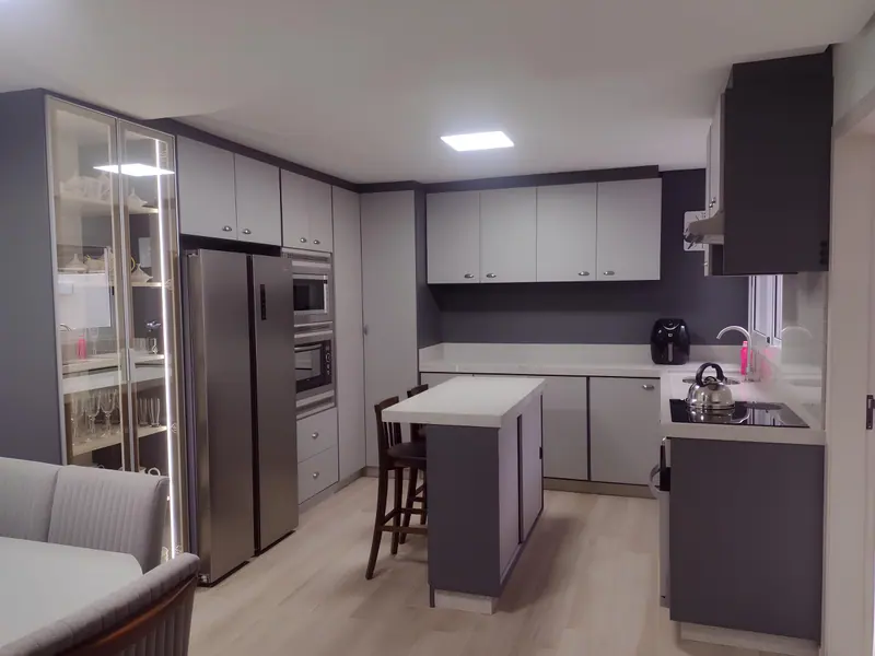 Cozinha planejada em tons de cinza com ilha central, cristaleira iluminada e armários até o teto