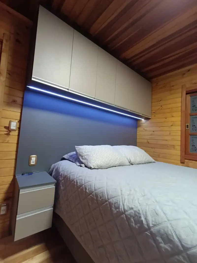 Dormitório em casa de madeira com armário aéreo sobre a cama e LED azul