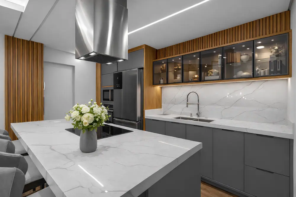 Cozinha planejada com ilha de tampo marmorizado, armários grafite, cristaleira com portas de vidro e painéis ripados em madeira